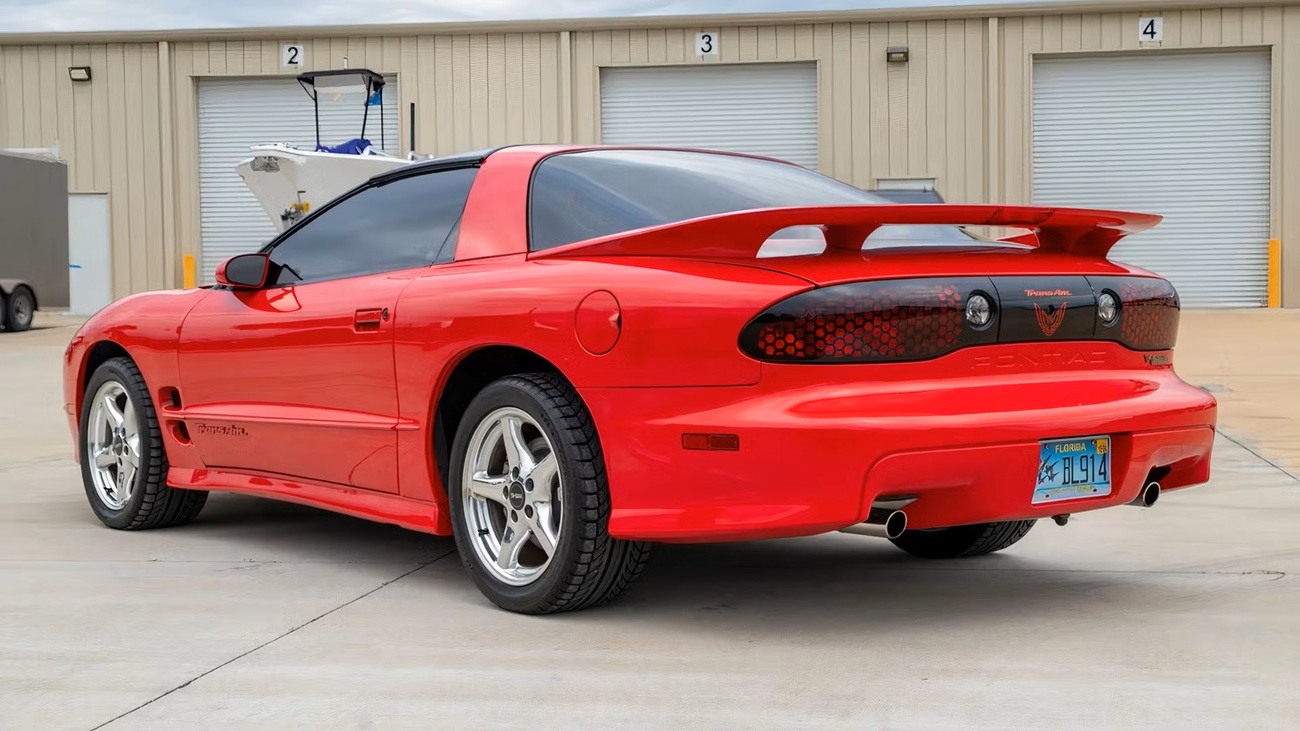 2001-pontiac-firebird-3 قرمز Pontiac Firebird Trans Am از عقب در یک پارکینگ با یک اسپویلر بزرگ عقب و پلاک فلوریدا دیده می شود.