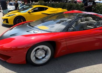 Red Ferrari LaFerrari with black hood and silver wheels, parked at a car show with a yellow sports car in the background and people strolling nearby.