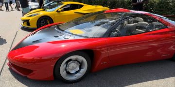 Red Ferrari LaFerrari with black hood and silver wheels, parked at a car show with a yellow sports car in the background and people strolling nearby.