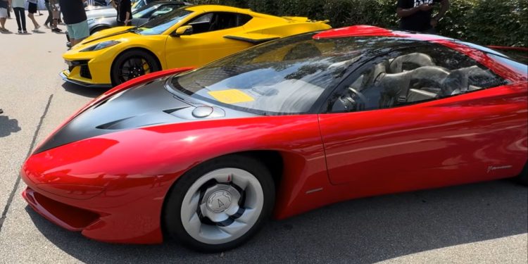 پونتیاک زمانی خودرویی را آنقدر پیشرفته ساخت که تولید آن توجیه اقتصادی نداشت 1 Red Ferrari LaFerrari with black hood and silver wheels, parked at a car show with a yellow sports car in the background and people strolling nearby.