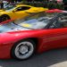 Red Ferrari LaFerrari with black hood and silver wheels, parked at a car show with a yellow sports car in the background and people strolling nearby.