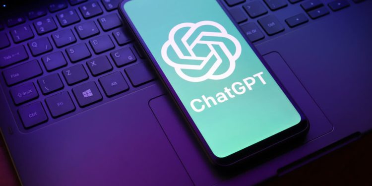 Phone showing the ChatGPT logo on a teal screen resting on a laptop keyboard.