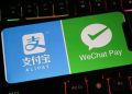 یک گوشی هوشمند روی صفحه‌کلید گیمینگ با نور پس‌زمینه رنگی که لوگوهای Alipay و WeChat Pay را روی نمایشگر خود نشان می‌دهد.