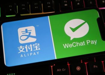 یک گوشی هوشمند روی صفحه‌کلید گیمینگ با نور پس‌زمینه رنگی که لوگوهای Alipay و WeChat Pay را روی نمایشگر خود نشان می‌دهد.