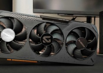 Triple‑fan graphics card from Gigabyte installed in a PC, visible heatsink and case side panel in the background, slogan 'Dominating the Games' on the card.