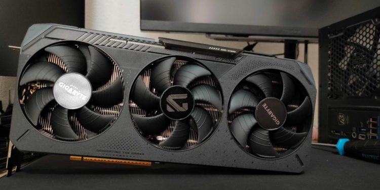 Triple‑fan graphics card from Gigabyte installed in a PC, visible heatsink and case side panel in the background, slogan 'Dominating the Games' on the card.