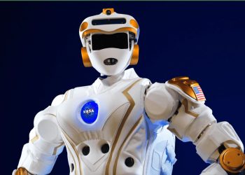 NASA humanoid robot in white armor with orange joints and a visible NASA logo on the chest, posed against a dark blue background.