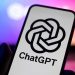 Card displaying the ChatGPT logo and name held in front of a blue‑pink neon background.