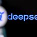 نمای نزدیک و تار از صفحه گوشی هوشمند که لوگو و نام آبی‌رنگ دیپ‌سیک (DeepSeek) را بر روی پس‌زمینه مشکی نمایش می‌دهد.