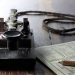 Vintage telegraph key with a coiled wire and a nearby instruction sheet on a dark wooden table, suggesting Morse code use