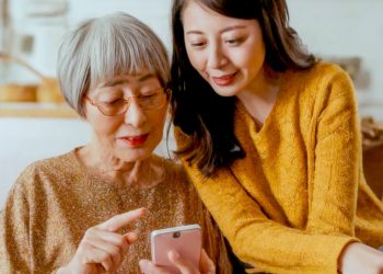 Two women, an elderly woman and a younger woman, look at a smartphone together.