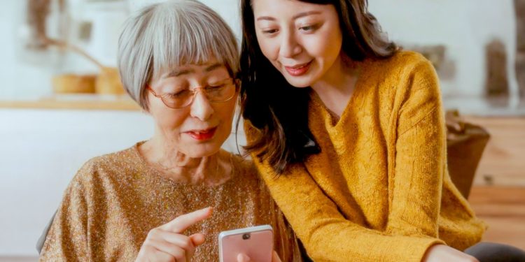 صدای شما ممکن است نشان دهد که چقدر سریع پیر می شوید 1 Two women, an elderly woman and a younger woman, look at a smartphone together.