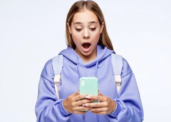 Young woman in a lavender hoodie and backpack looks surprised while checking her mint green smartphone.