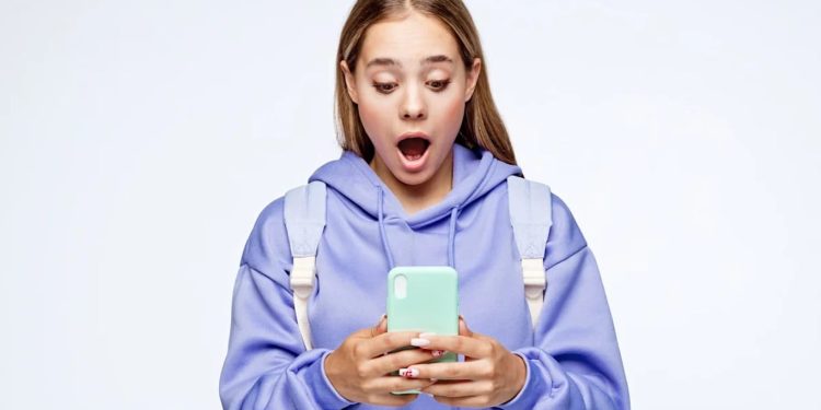 Young woman in a lavender hoodie and backpack looks surprised while checking her mint green smartphone.