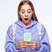 Young woman in a lavender hoodie and backpack looks surprised while checking her mint green smartphone.