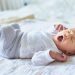 چرا هفته اول زندگی ممکن است برای سلامت آینده کودک مهم باشد؟ 8 Yawning newborn baby lying on a light blanket, wearing white pajamas with small stars.