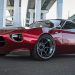 تویوتا اسپورت 800 با ظاهری مدرن بازگشته است 8 Low-angle view of a glossy red sports coupe with wide aftermarket wheels parked under an elevated highway pillar area in an urban setting.