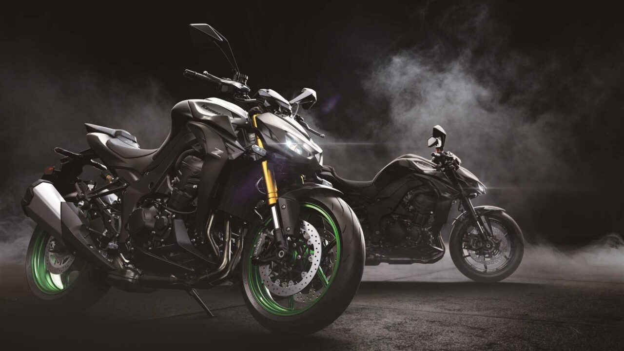 دو موتور سیکلت اسپرت در یک پس زمینه تاریک و دودی؛ دوچرخه پیش‌زمینه دارای رینگ‌های سبز روشن و چنگال‌های جلوی طلایی است، آرم روی مخزن قابل مشاهده است.»