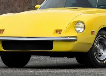Front view of a bright yellow vintage sports car, showing round headlight, chrome bumper, and curved body lines on a pavement surface.