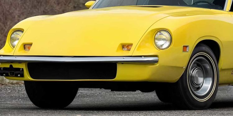 Front view of a bright yellow vintage sports car, showing round headlight, chrome bumper, and curved body lines on a pavement surface.
