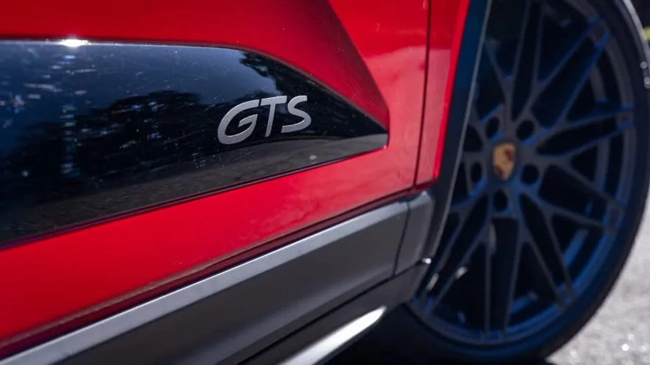 1000084824 نمای نزدیک از یک خودروی اسپرت قرمز با نشان پانل جانبی مشکی با خواندن «GTS» و یک چرخ چند پره آبی در پسزمینه (پورشه).