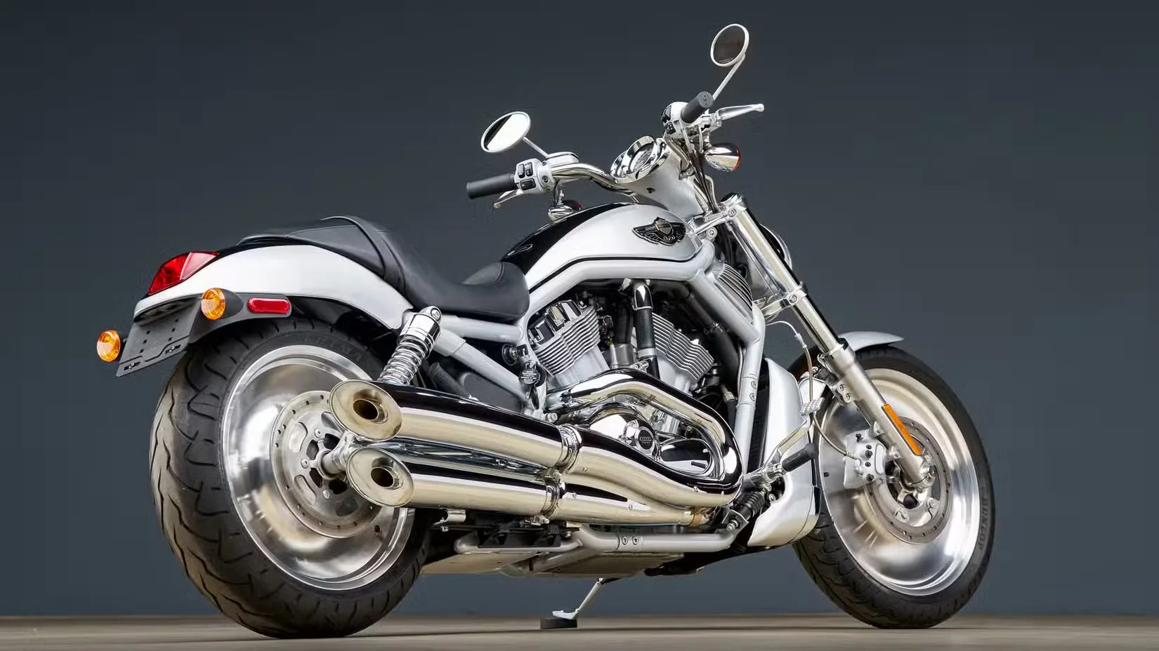 Silver chrome motorcycle photographed from the left-rear side, parked on a flat surface against a dark gradient background.