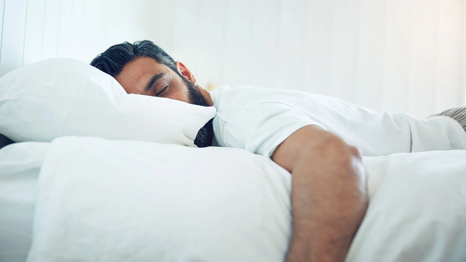 This is what weekends were made for Bearded man sleeping on a white pillow in a bright bedroom.