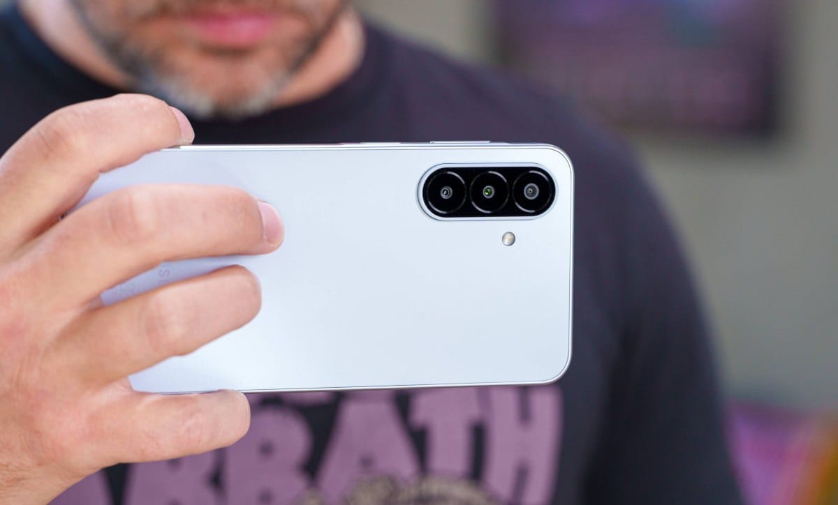 gsmarena_101 Hand holding a white smartphone showing its triple-camera rear setup and flash on the back.