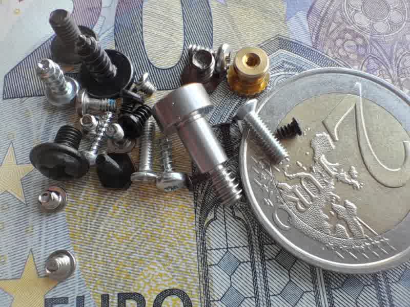 gsmarena_6101 Assorted screws, bolts, and fasteners scattered on a 1-euro coin and euro banknote for scale.