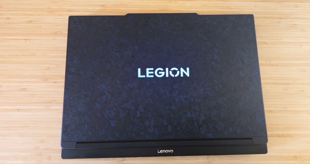 1000085046 نمای بالا به پایین یک لپتاپ بسته Lenovo Legion روی سطح چوبی سبک، نشانواره مرکزی قابل مشاهده است.