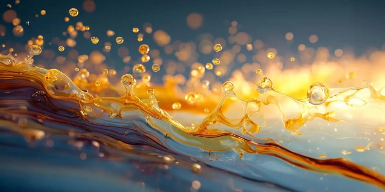 Golden liquid splashes across a blue surface with glowing droplets and a warm sunset glow in the background.