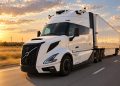 White semi-truck with trailer driving on a highway at sunset, emphasizing motion and warm sky colors.