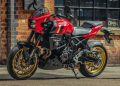 Red Suzuki sport motorcycle with gold wheels parked beside a brick storefront exterior.