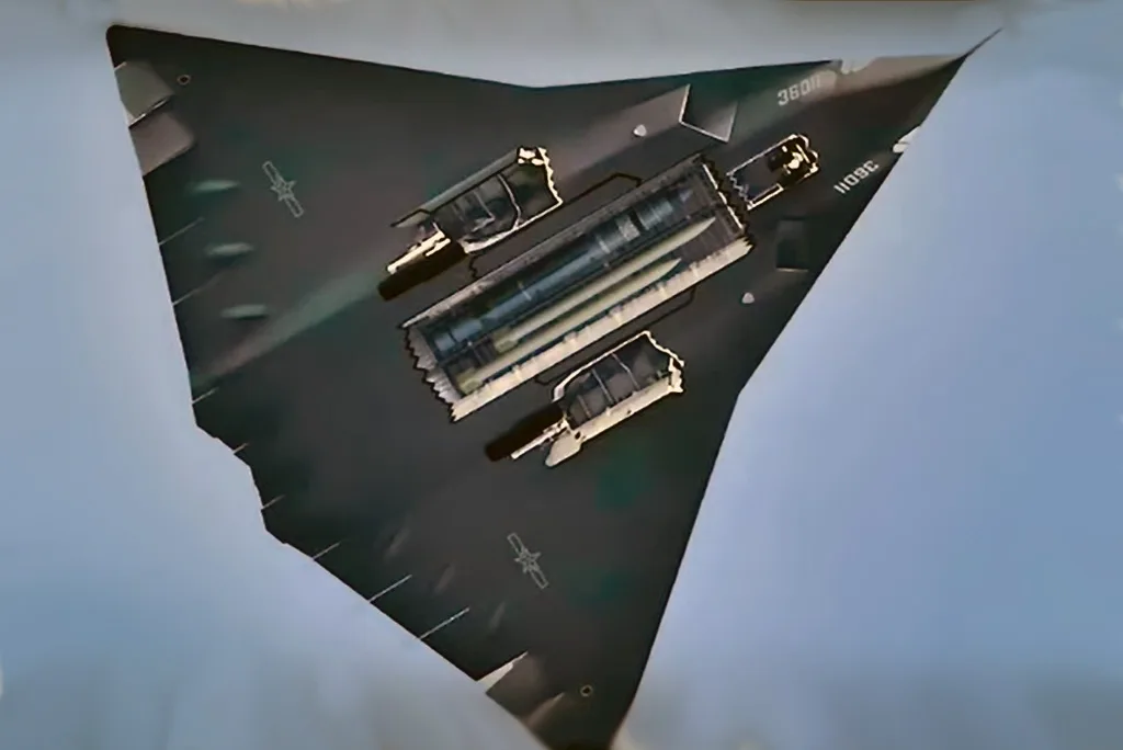 نمای بالا به پایین یک بمب افکن رادارگریز B-2 Spirit با مهمات خارجی بارگذاری شده، که در آسمان آبی روشن پرواز می کند.