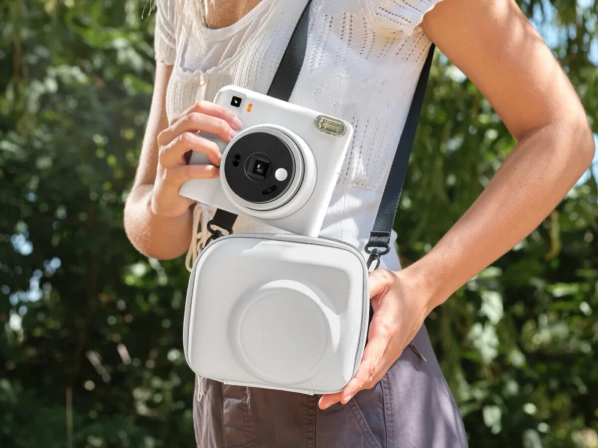 Fujifilm's Instax Square 2 camera was introduced with creative filters 5 A person in a white summer dress and a white duffle bag is holding a white Instax Square SQ2 instant print camera with a black strap around his neck and hands.
