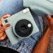Fujifilm's Instax Square 2 camera was introduced with creative filters 7 نمای بالای فردی نشسته با شلوار جین آبی که یک دوربین چاپ سریع آبی پاستلی Instax Square SQ2 و کیف محافظ همرنگ آن را روی پای خود نگه داشته است.