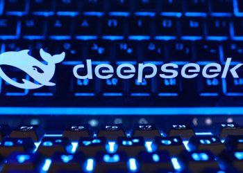 ایالات متحده استفاده از DeepSeek را در سازمان های دولتی ممنوع کرد 2 لوگو و نوشتهی دیپسیک روی صفحهنمایش لپتاپ در کنار کیبورد با نور پسزمینهی آبیرنگ.