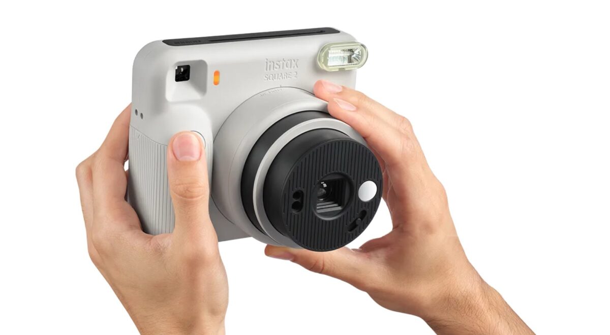 Fujifilm's Instax Square 2 camera was introduced with creative filters 4 Two hands holding a light gray Instax Square SQ2 instant camera for photography, with focus on the keys, black rotating lens and top flash on a white background.