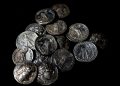 Pile of ancient silver coins scattered on a black background, showing portraits and inscriptions.