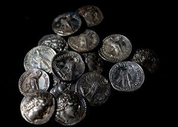 Pile of ancient silver coins scattered on a black background, showing portraits and inscriptions.