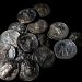 Pile of ancient silver coins scattered on a black background, showing portraits and inscriptions.