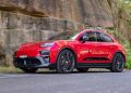 Red Porsche SUV (Macan) parked on a paved road beside a rocky wall with greenery in the background.