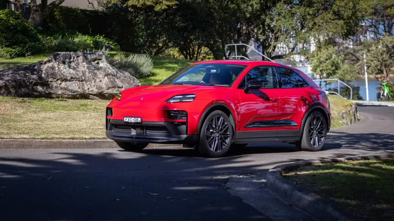 1000084833 شاسی بلند قرمز پورشه در خیابانی حومه شهر با فضای سبز و صخره در پس زمینه پارک شده است.