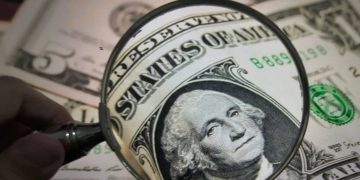 نگاه از پشت ذره‌بین به پرتره‌ی جورج واشنگتن روی اسکناس یک دلاری آمریکا.