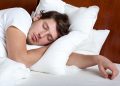 Young man sleeping on white pillows in a bed with a wooden headboard