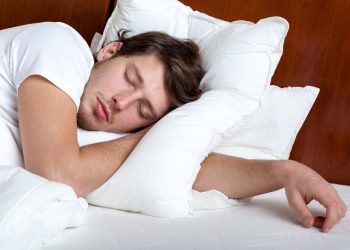 Young man sleeping on white pillows in a bed with a wooden headboard
