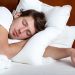 Young man sleeping on white pillows in a bed with a wooden headboard