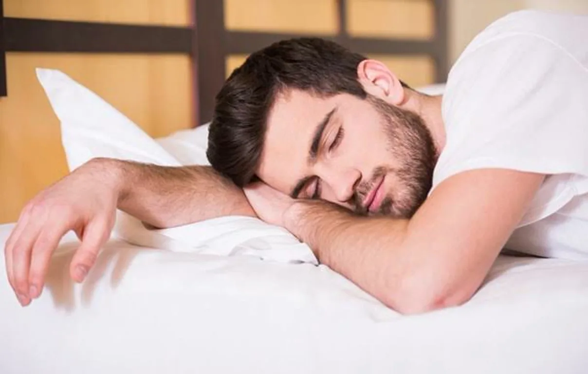 1000084735 Man with dark hair and beard sleeping on a white pillow on a bed in a bedroom