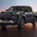 Dark gray Toyota Hilux BEV pickup shown in a studio with a warm sunset gradient background, angled front-left view
