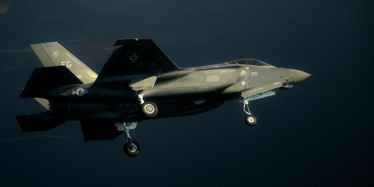 حسگر لیزری چینی موفق شد جنگنده F-35 آمریکایی را شناسایی کند 1 F-35 stealth fighter jet in mid-flight over the ocean with landing gear down, side view of a gray military aircraft.